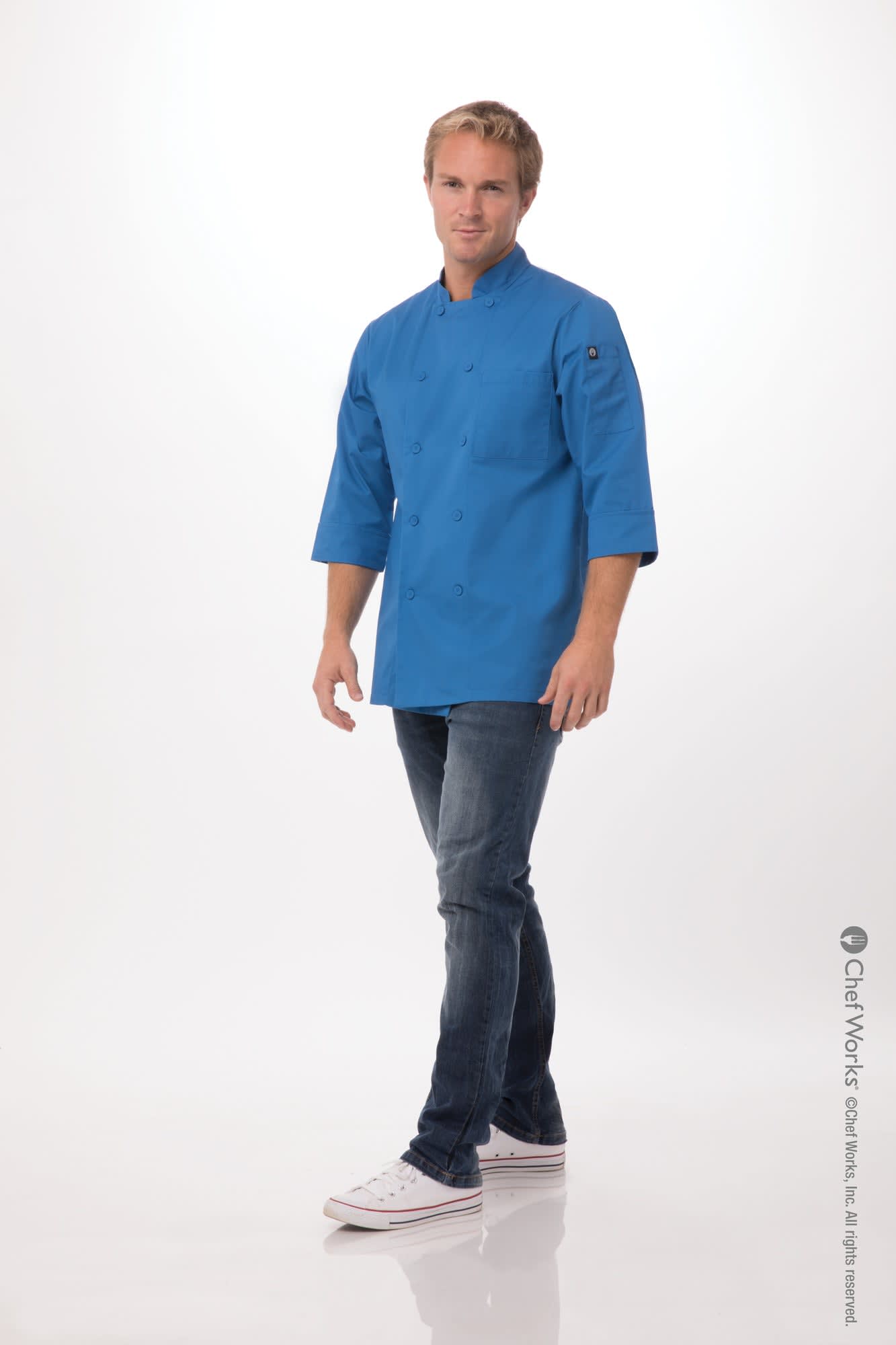 A man wearing a bright blue chef jacket with three-quarter sleeves, paired with jeans and white sneakers.