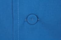 A blue men's chef jacket featuring a button detail and stitching. It includes a logo on the fabric.