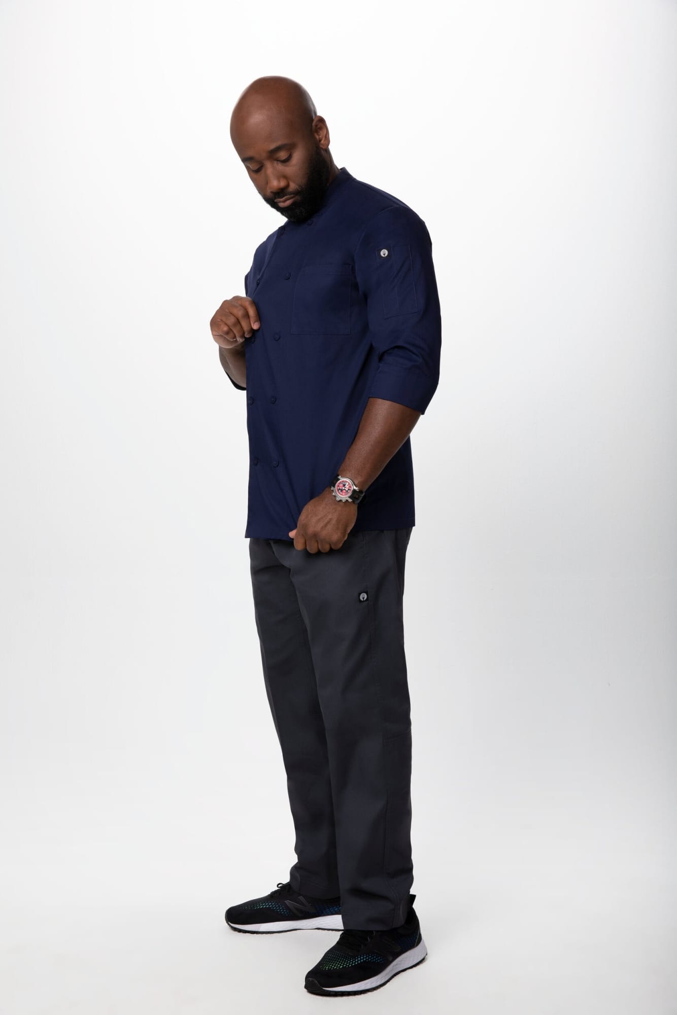 A men's chef jacket in navy blue, paired with black pants, worn by a man standing confidently. The outfit features a logo.