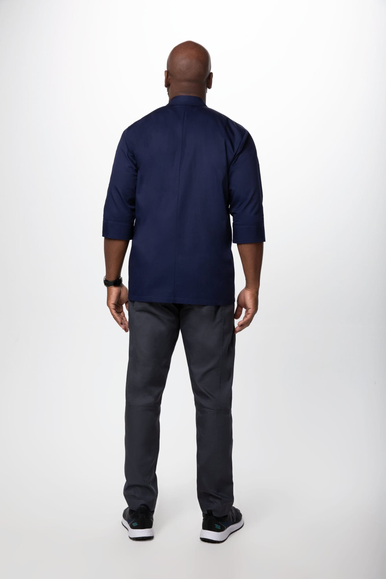 A navy men's chef jacket with a tailored design, worn with grey pants and black shoes. The model is shown from the back.