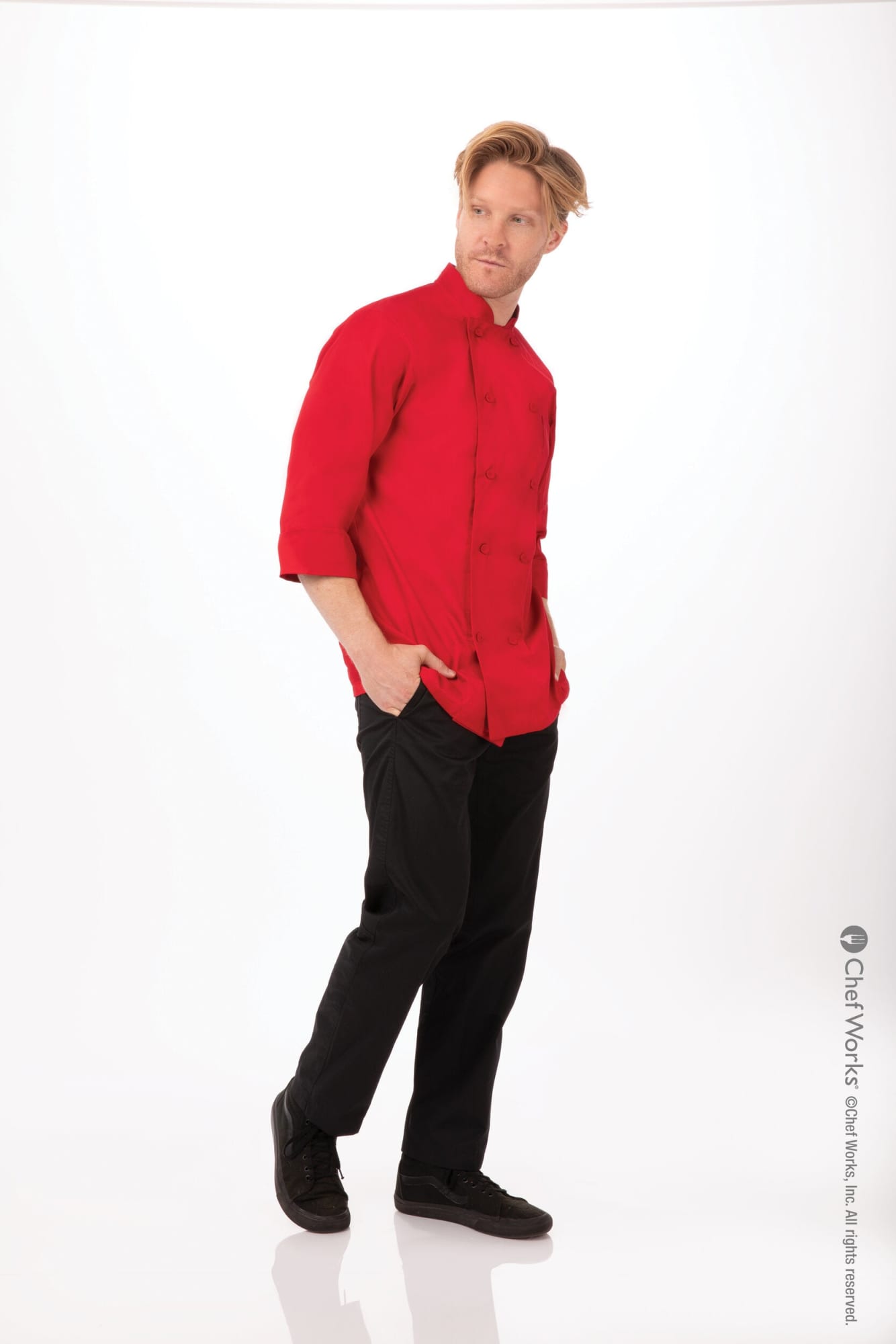 A man wearing a red chef jacket and black pants, posing against a white background. The outfit has a logo.