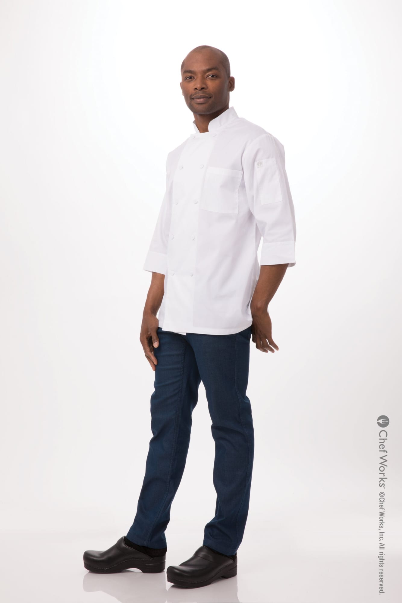 A men's chef jacket in white, paired with dark blue jeans, worn by a model standing against a light background.