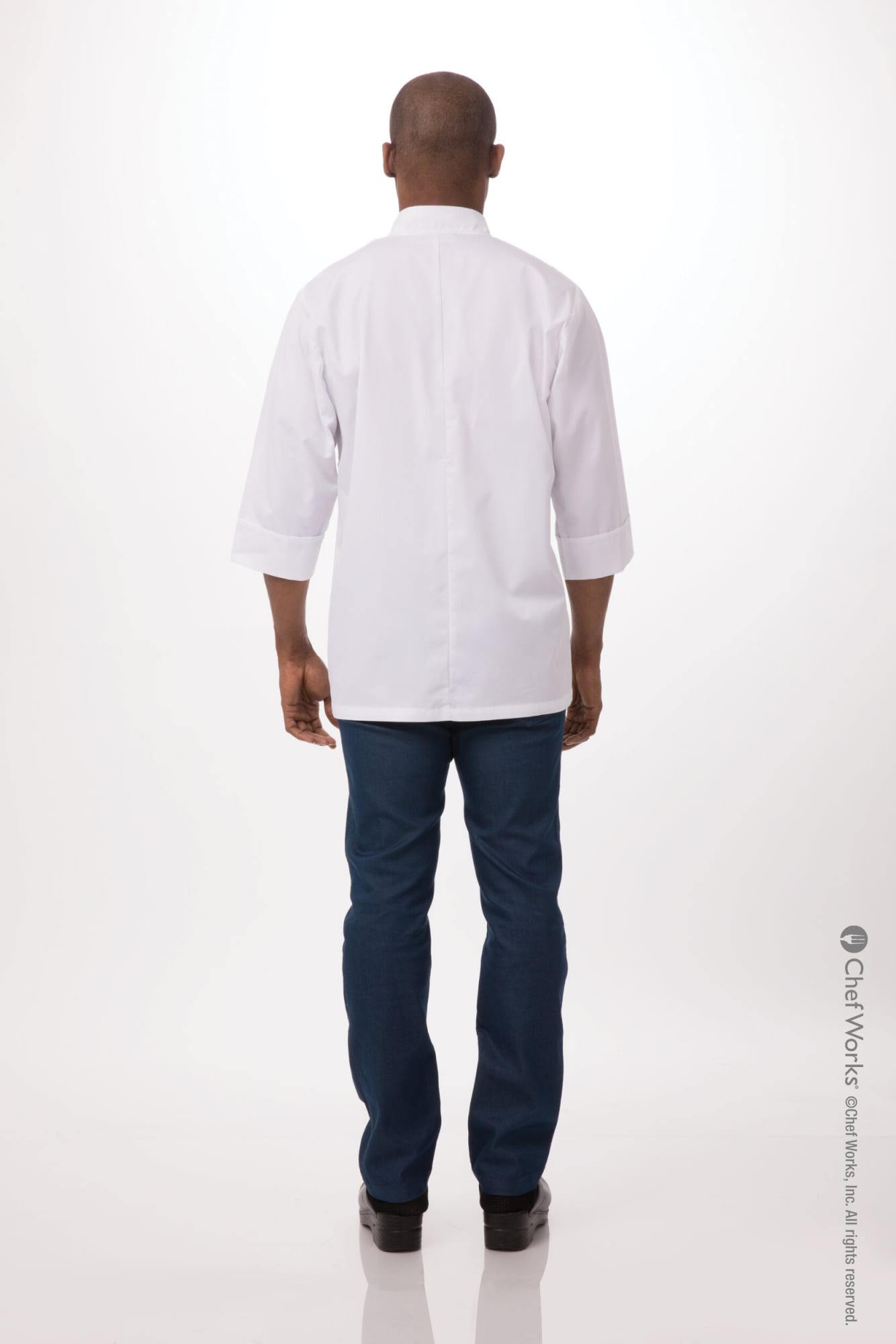 A man in a plain white chef jacket and dark blue pants, viewed from the back. The jacket has a logo.