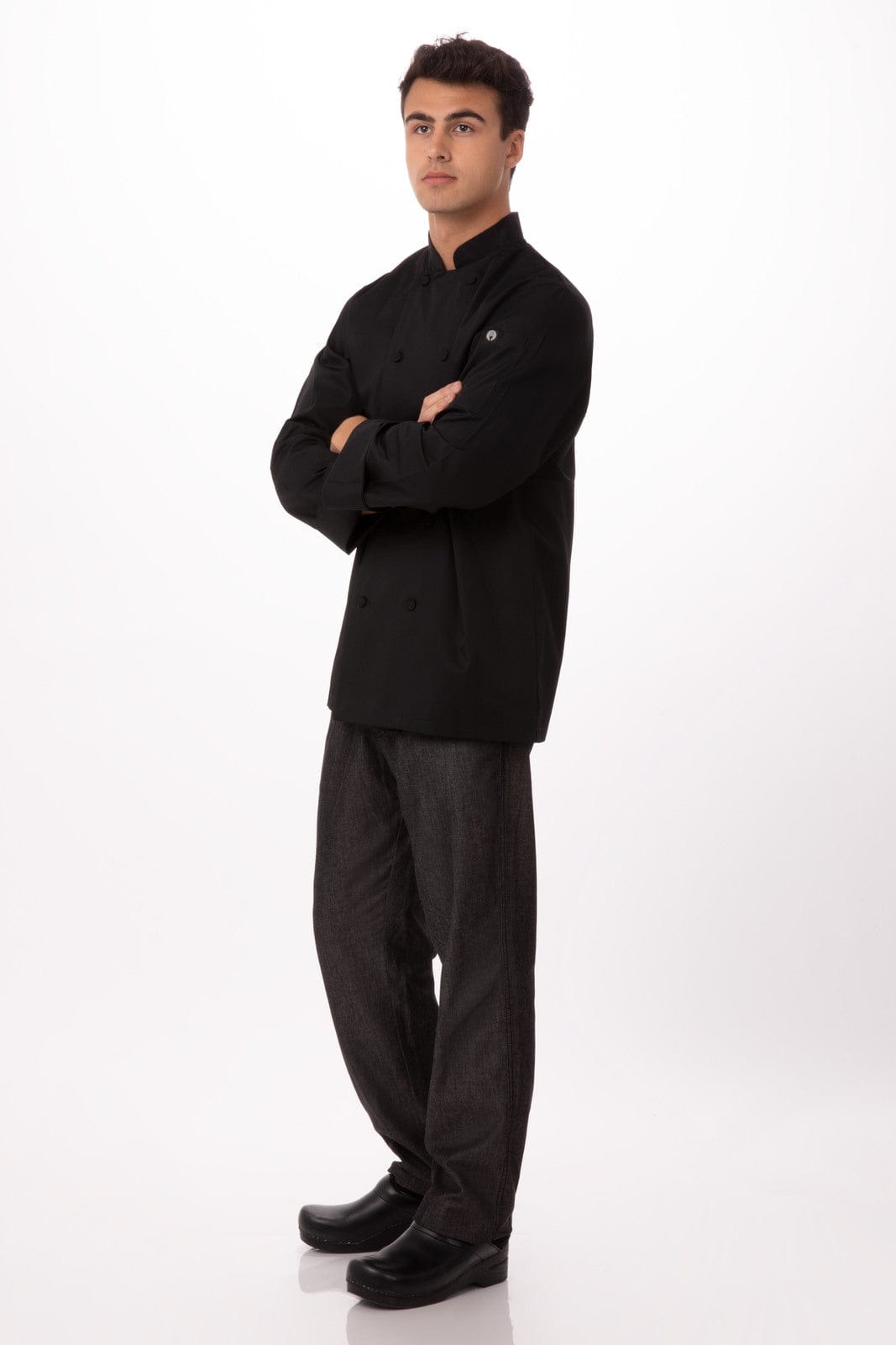 A black chef jacket worn by a man standing with arms crossed, paired with dark trousers and footwear.
