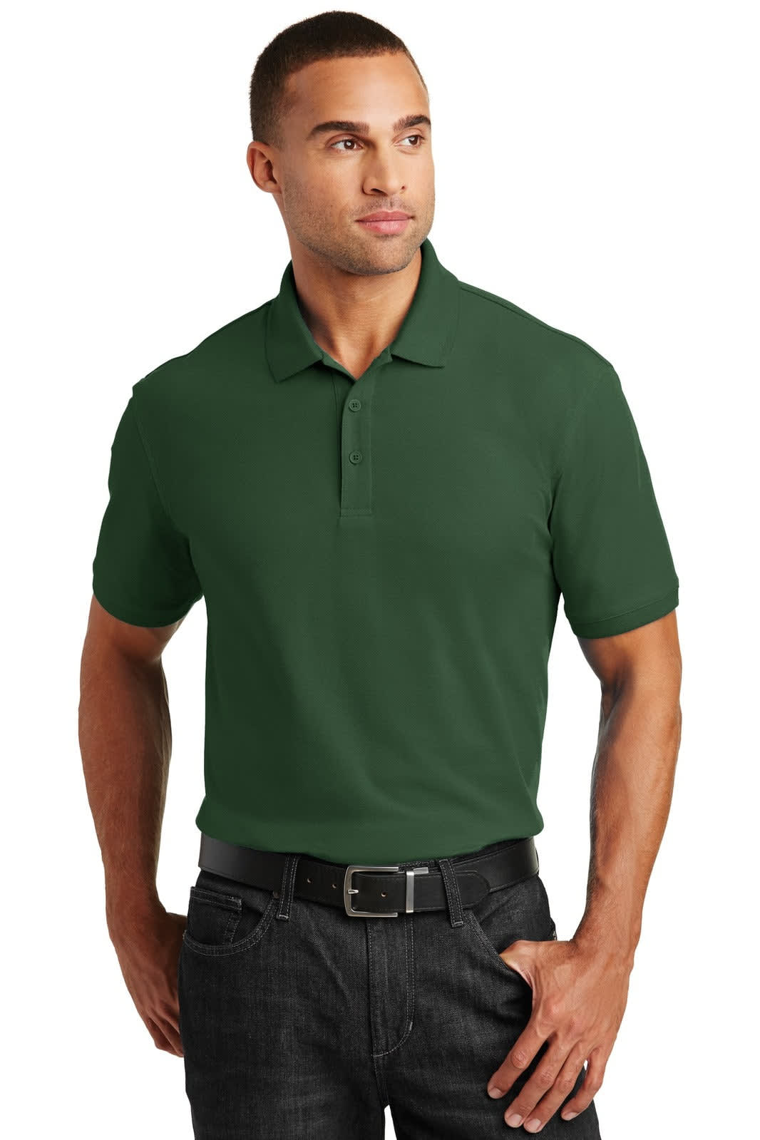A man wearing a dark green polo shirt stands with his hands in his pockets, featuring a logo on the chest.