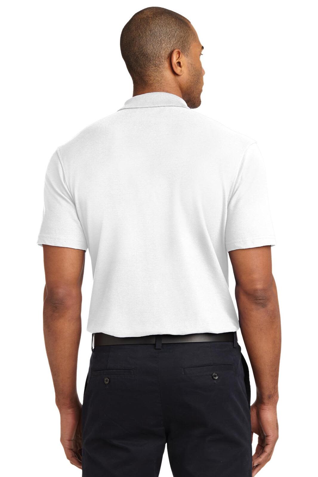 A man wearing a white Port Authority stain-resistant polo shirt, viewed from the back, paired with dark trousers.
