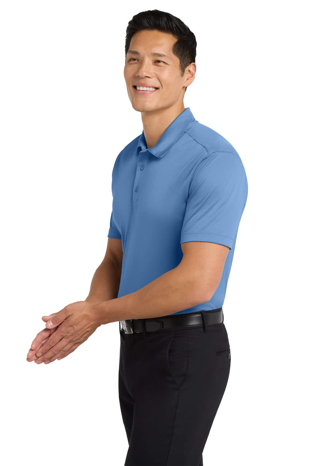 A man wearing a light blue polo shirt stands smiling, paired with black trousers. The shirt features a logo.