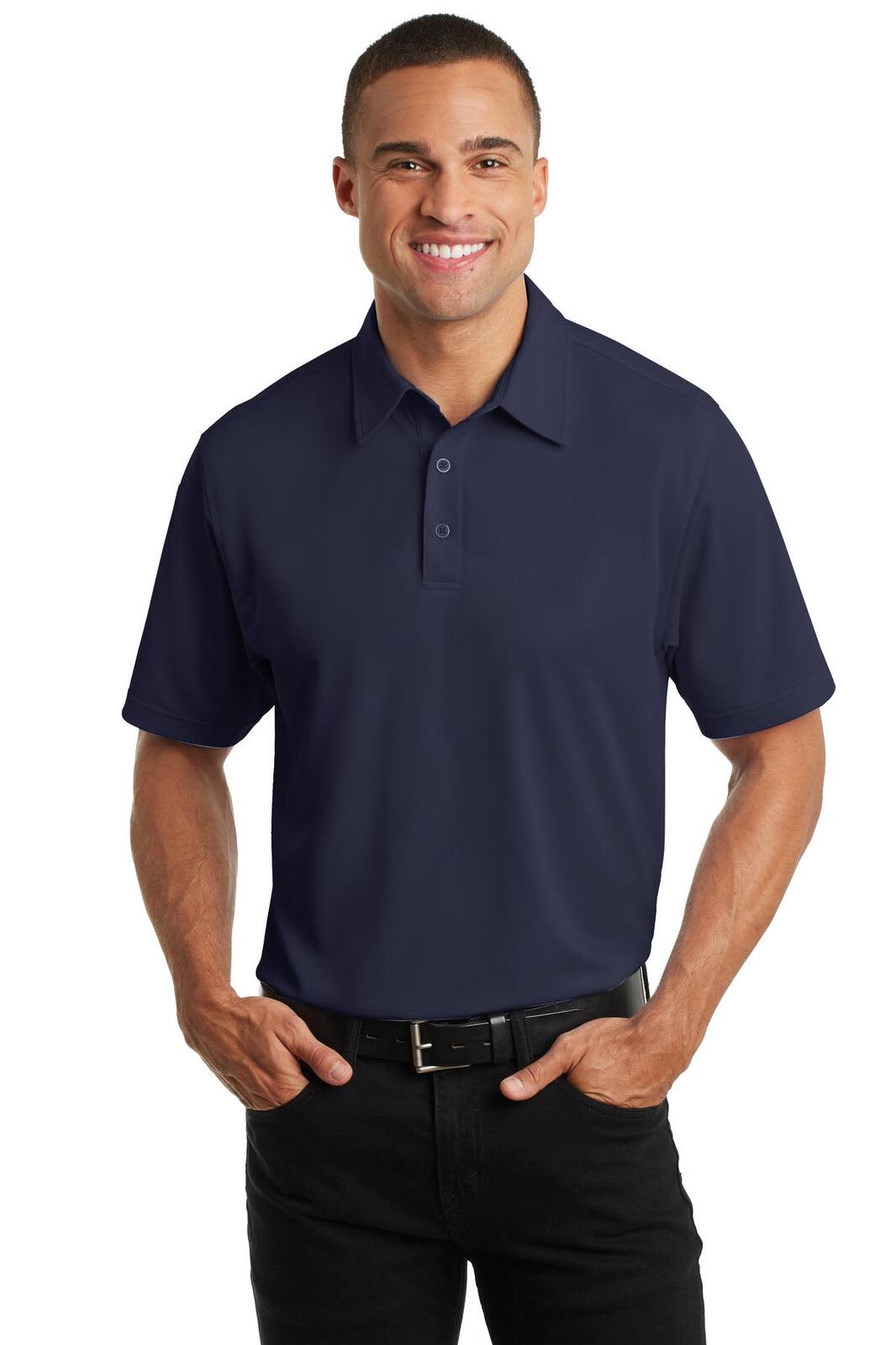 A man wearing a navy blue Port Authority Dimension Polo shirt, with a collar and short sleeves, standing with hands in pockets.