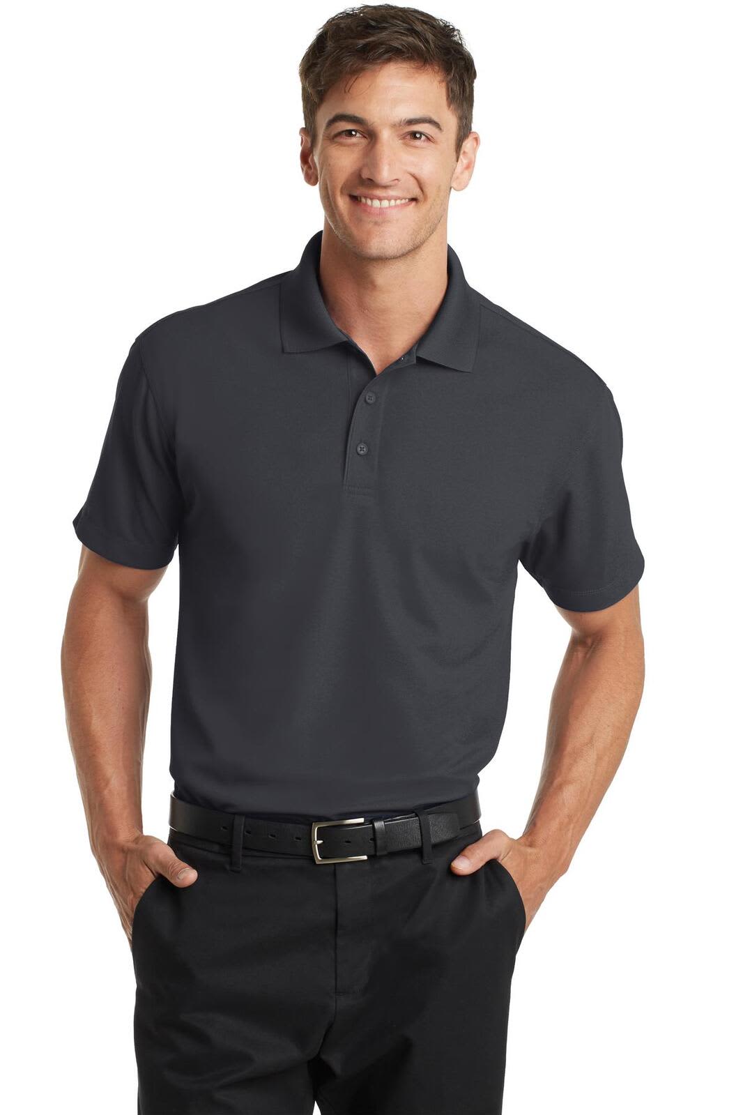 A man wearing a charcoal grey polo shirt, standing with hands on hips and smiling, featuring a logo on the chest.