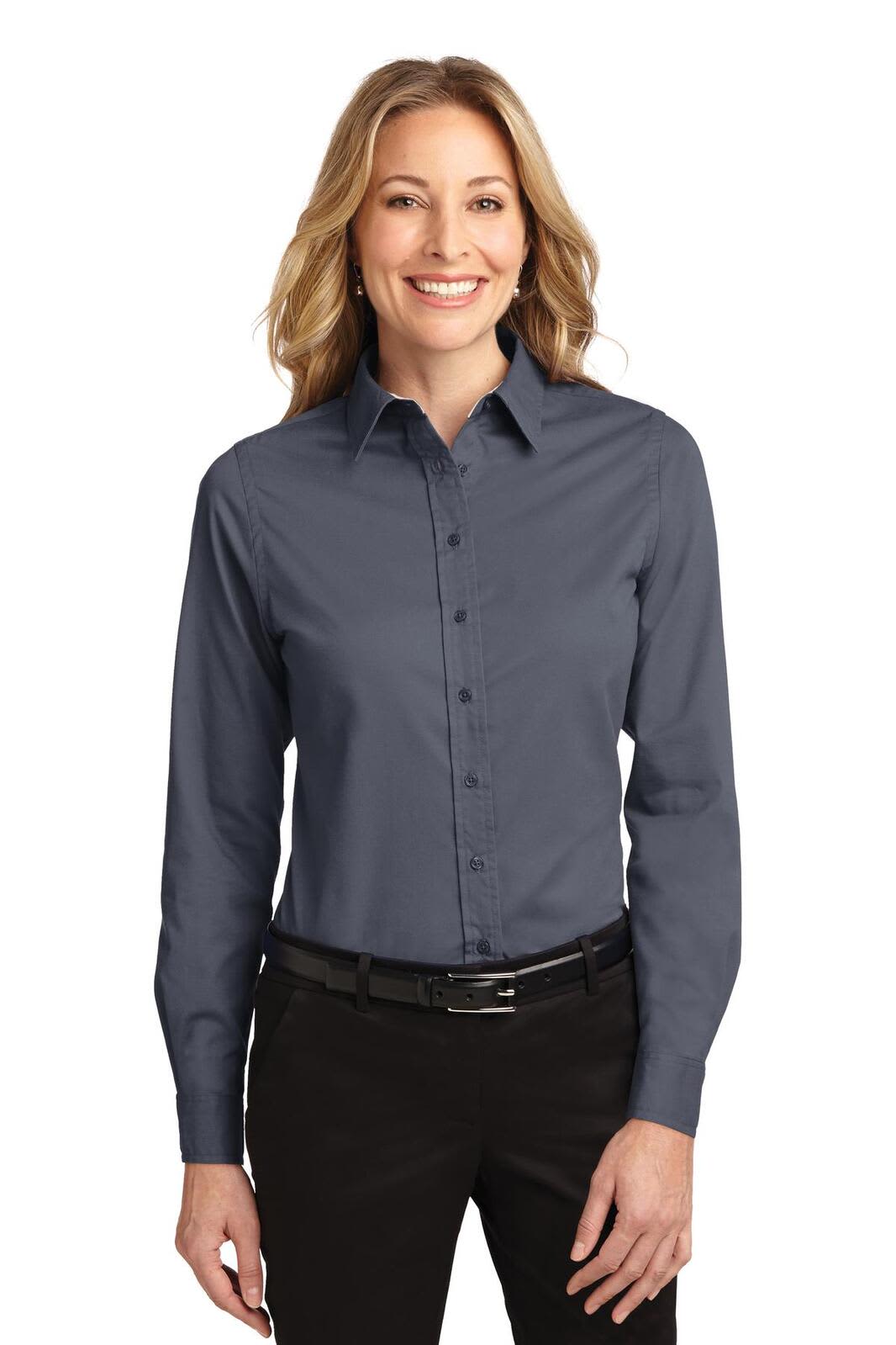 A long-sleeve button-up shirt in dark navy blue, featuring a collar and a logo. Model wears it with black trousers.
