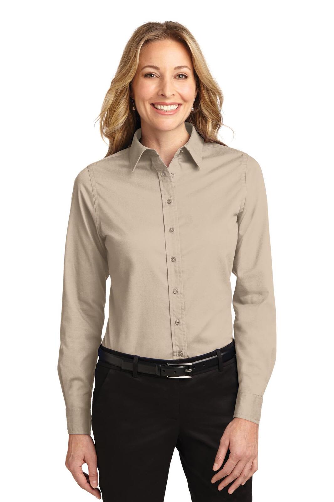 A smiling woman wearing a beige long-sleeve button-up shirt, styled with a black belt and dark pants.