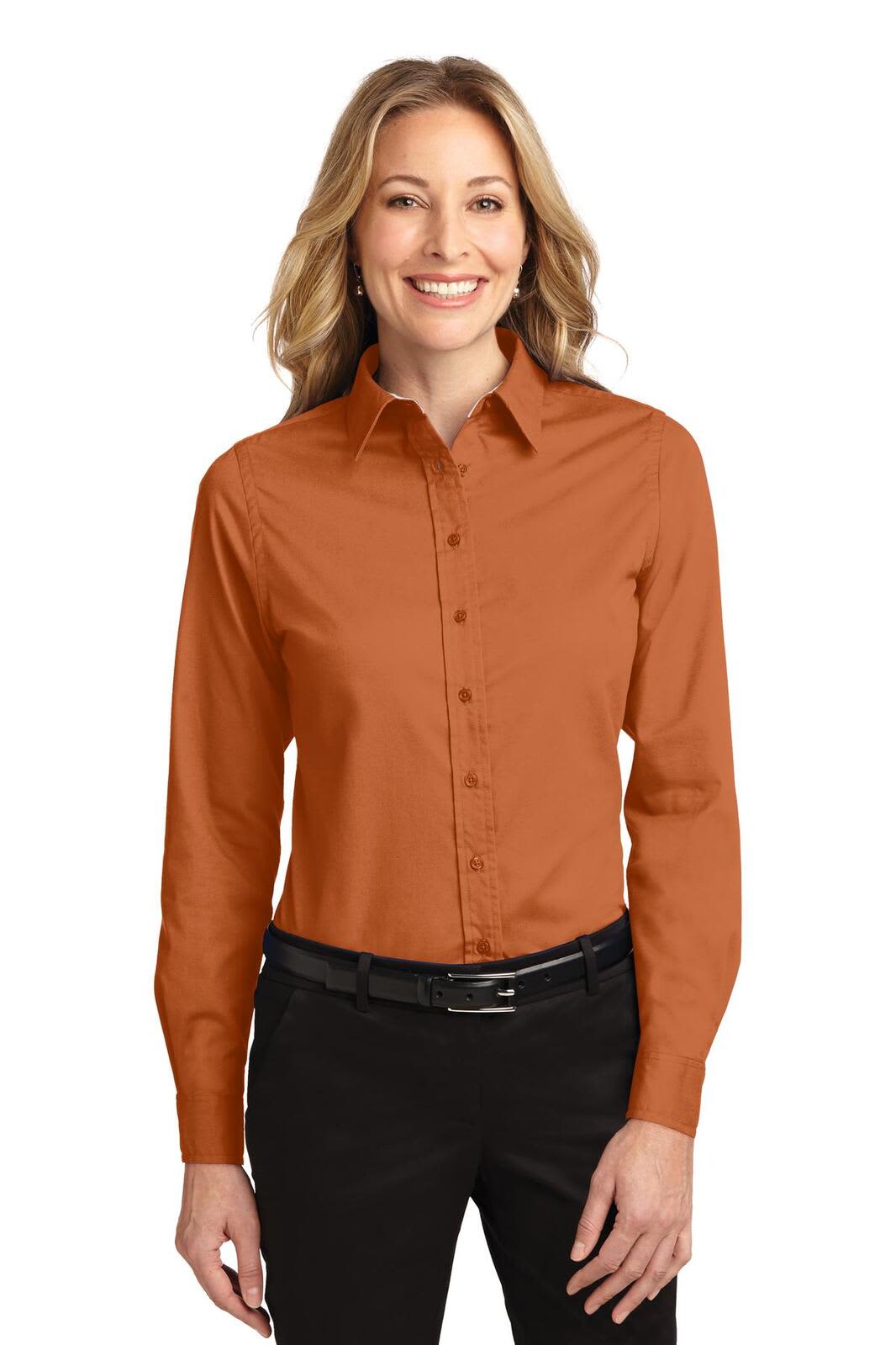 A woman wearing a long sleeve button-up shirt in burnt orange, paired with black pants. The shirt includes a logo.