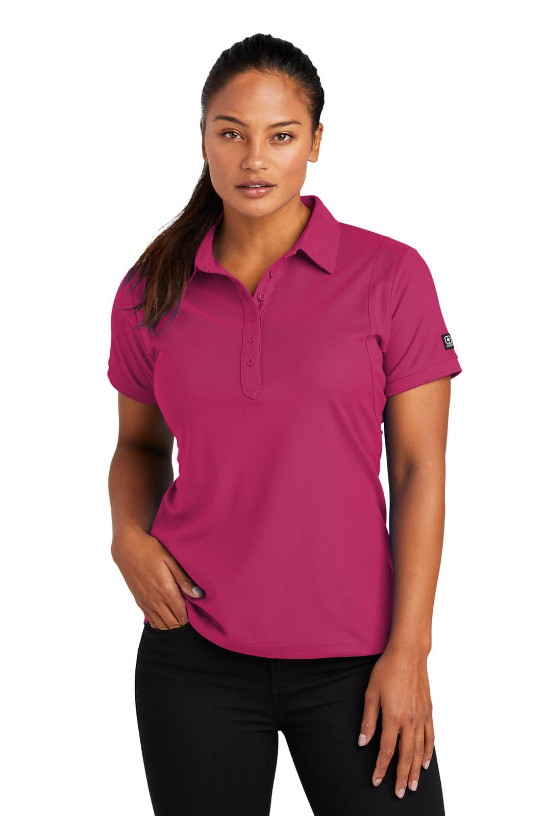 A woman is wearing a pink OGIO Jewel Polo shirt. The shirt features a logo on one sleeve.