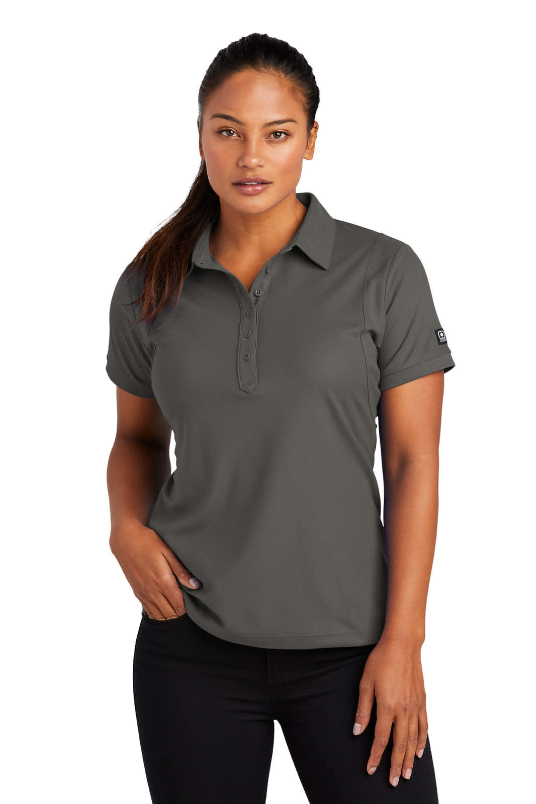 A woman wearing a dark grey polo shirt with a logo on the sleeve, posing confidently with one hand on her hip.