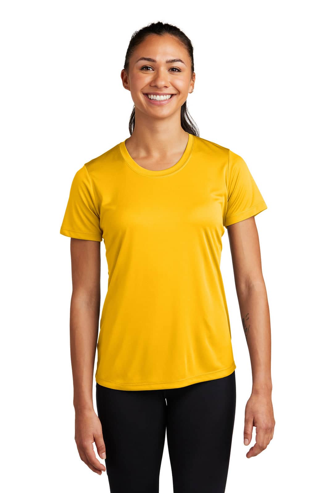 A woman stands smiling in a vibrant yellow Sport-Tek Ladies PosiCharge Competitor Tee, paired with black leggings.