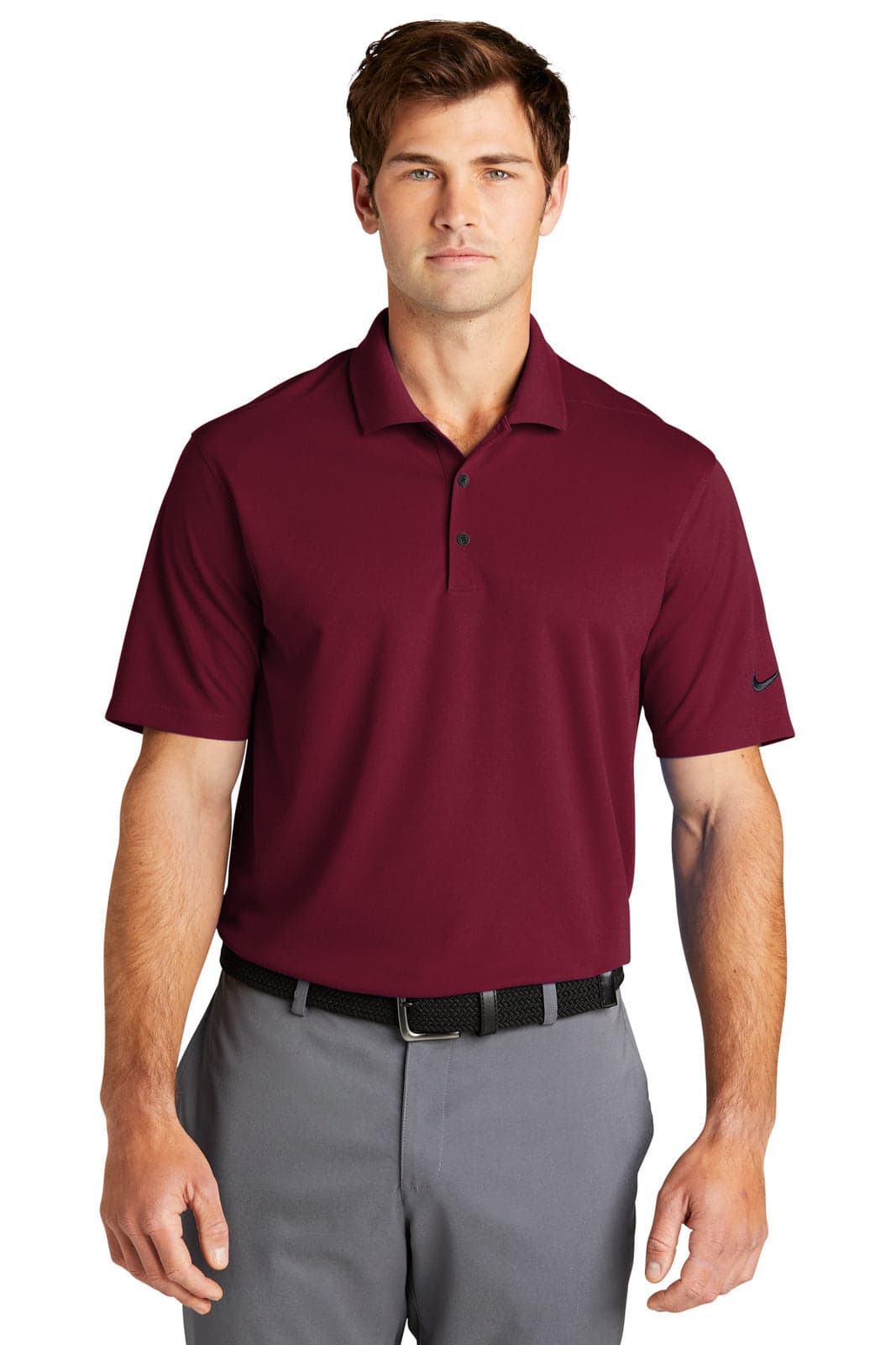 A man in a burgundy polo shirt stands, wearing grey trousers and a black belt. The polo features a logo on the sleeve.