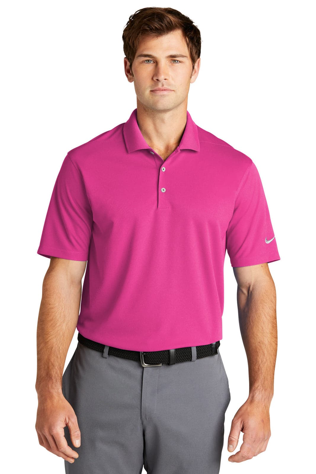 A man models a bright pink Nike Dri-FIT Micro Pique 2.0 Polo shirt, paired with grey trousers. The shirt features a logo.