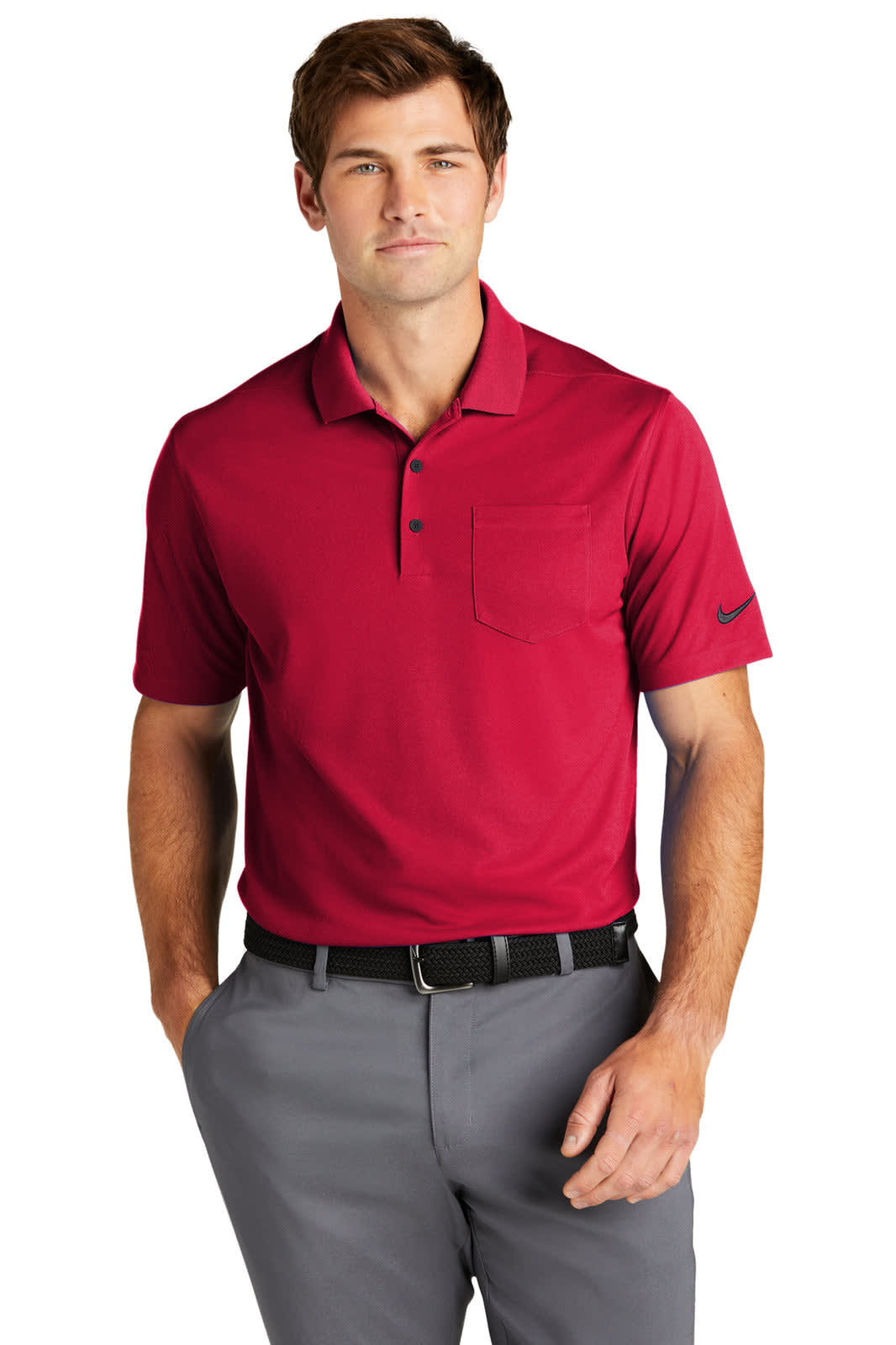 A man is wearing a red Nike Dri-FIT Micro Pique 2.0 Pocket Polo with a logo on the sleeve and grey trousers.