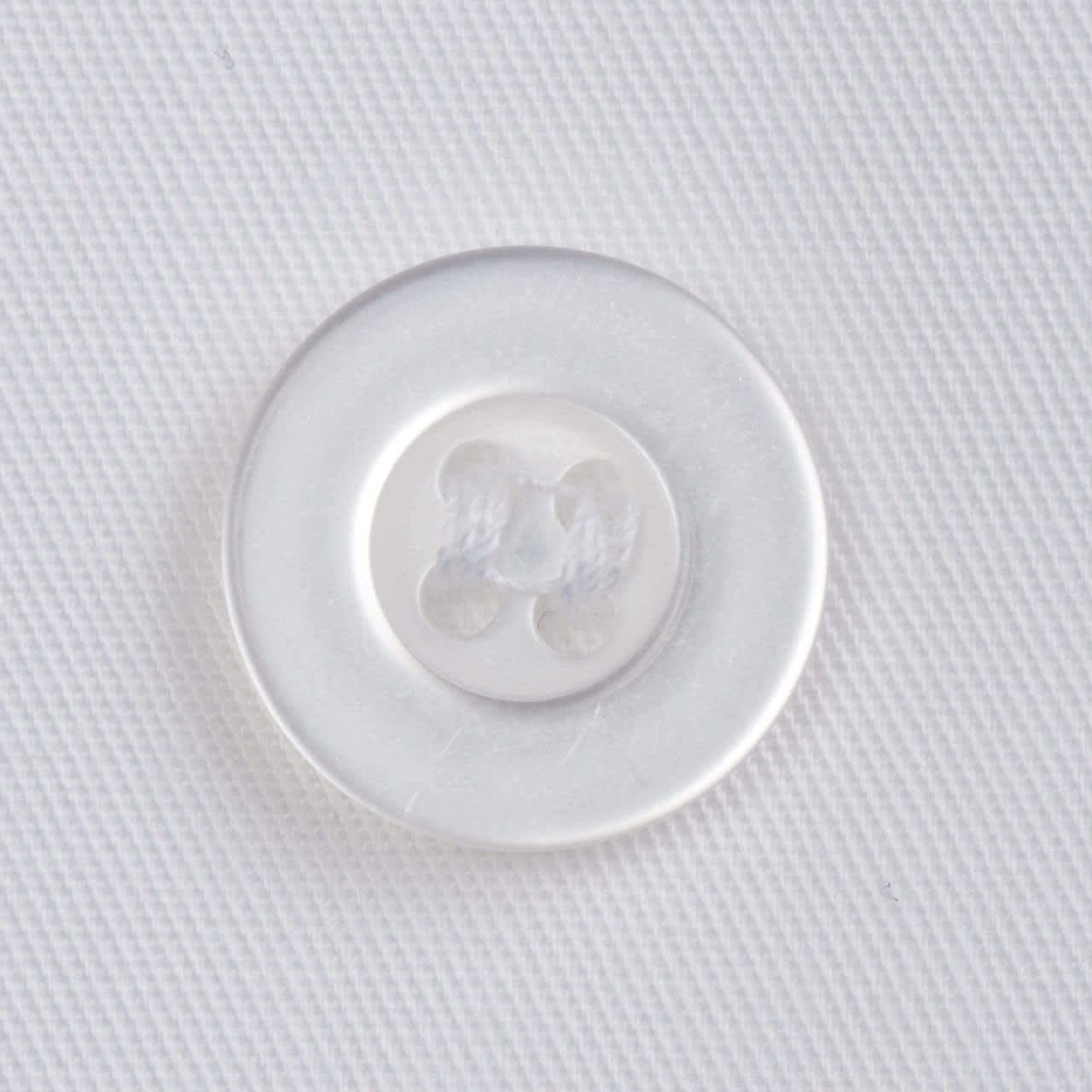 A clear circular button with four holes, set against a textured white fabric background.