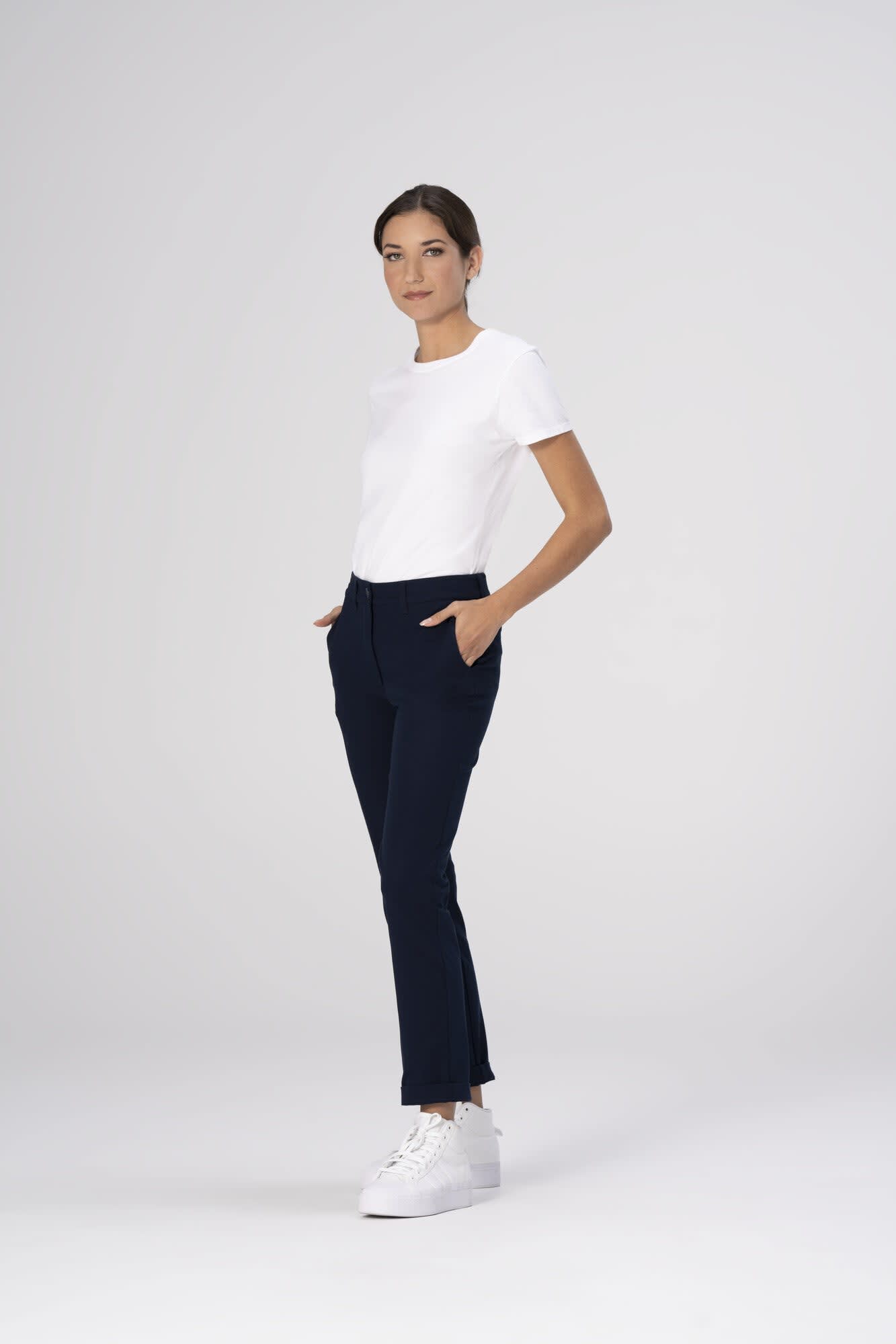 A model wearing navy Chino women's poly stretch pants paired with a white t-shirt and white sneakers, featuring pockets.