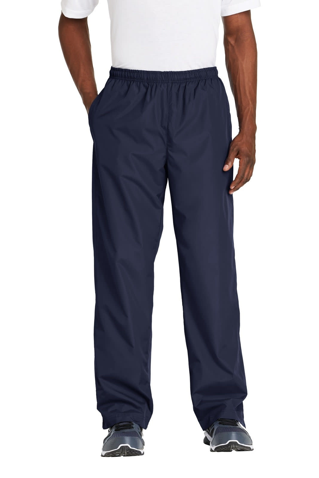 Navy track pants with an elastic waistband and side pockets, featuring a logo. Model stands with hands in pockets.