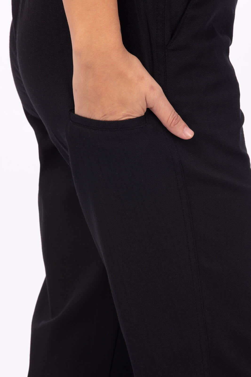 A close-up of black chef pants featuring a hand in the side pocket. Logos are visible on the fabric.