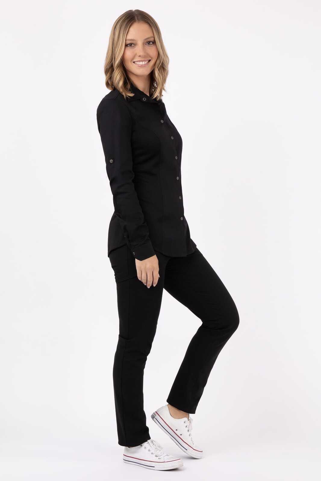 A woman in a black Seville shirt poses against a plain background, paired with black pants and white sneakers.