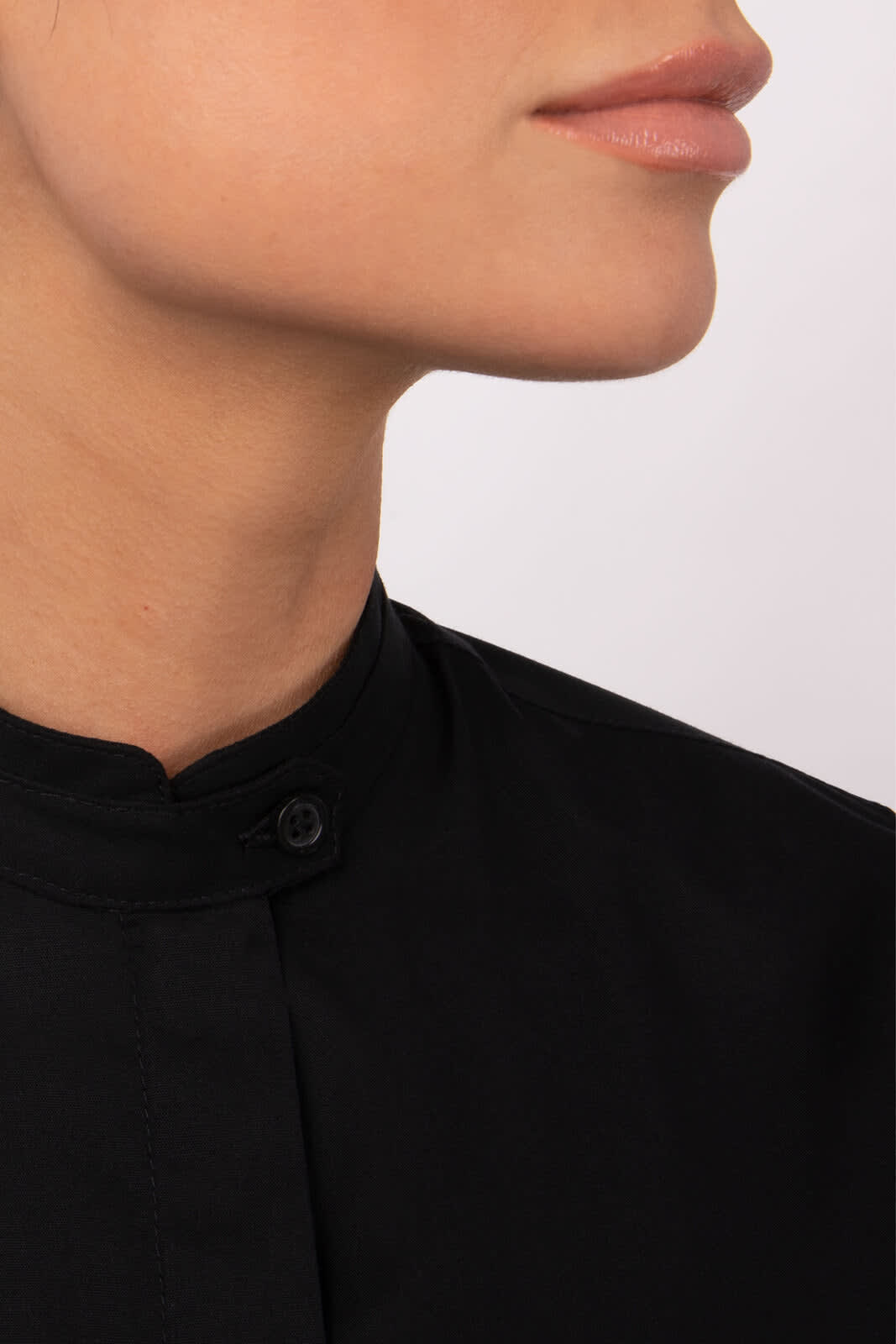 A close-up of a woman's neck and chin wearing a black button-up shirt with a collar and a small logo.