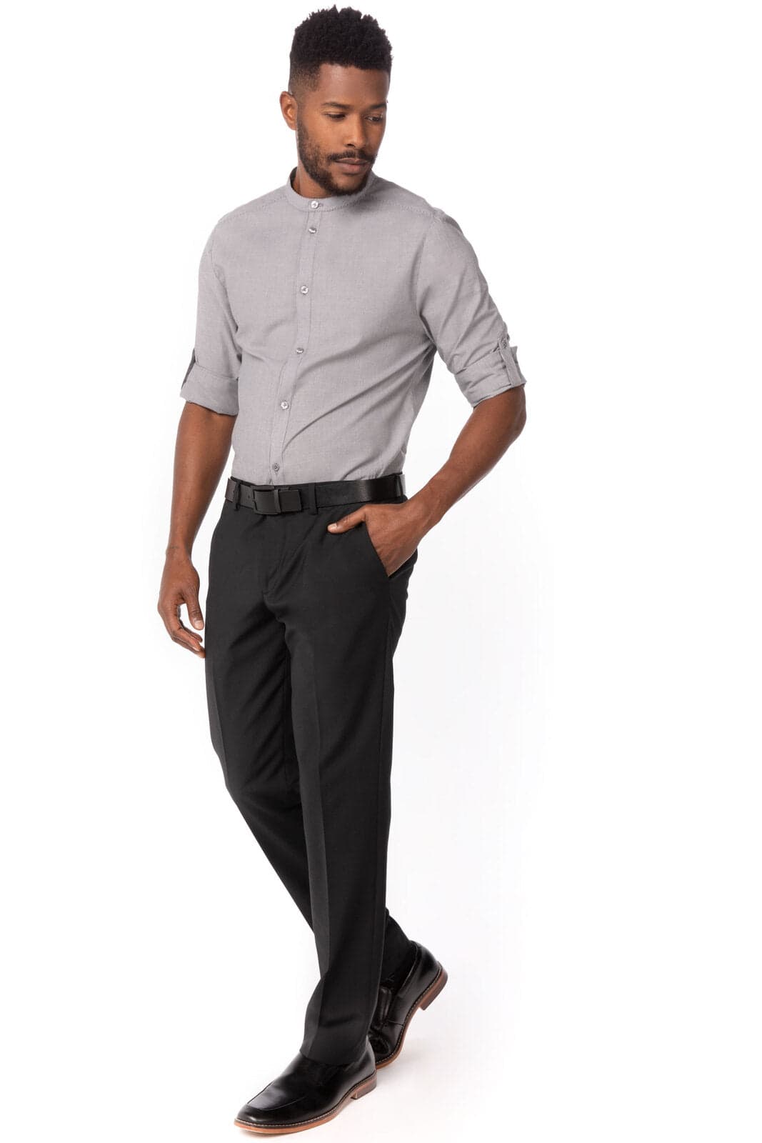A man wearing a grey button-up shirt and black trousers, standing casually with one hand in his pocket.
