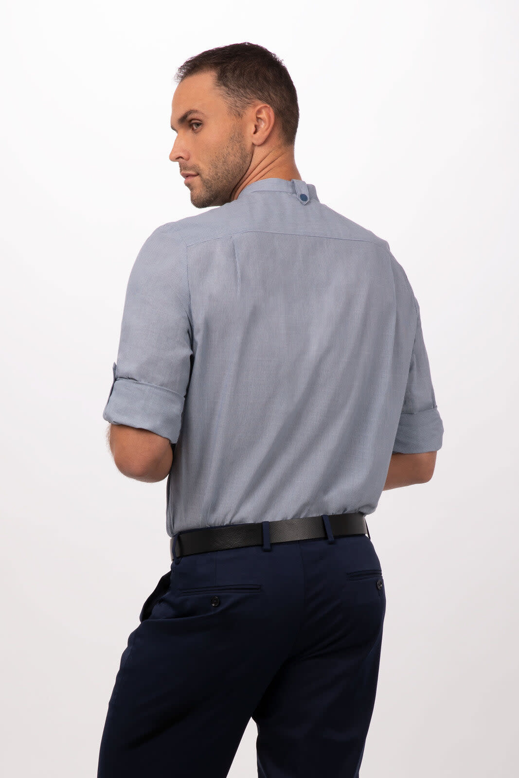 A man wearing a light blue button-up shirt with rolled sleeves, featuring a branding logo, viewed from the back.