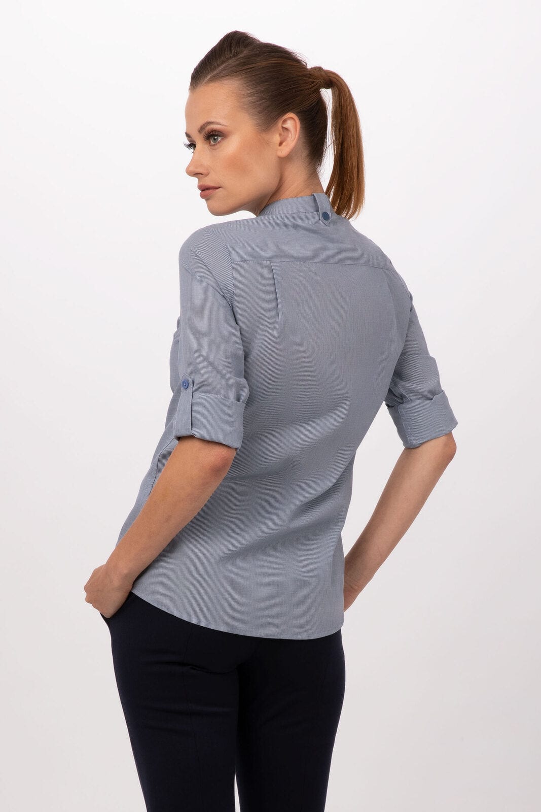 A woman in a light blue button-up shirt, featuring rolled sleeves and a fitted design, with her back turned to the camera.