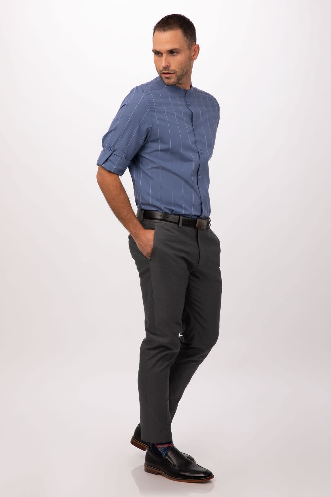 A men's button-up shirt in blue with stripes, paired with grey trousers. Model stands with hands in pockets.