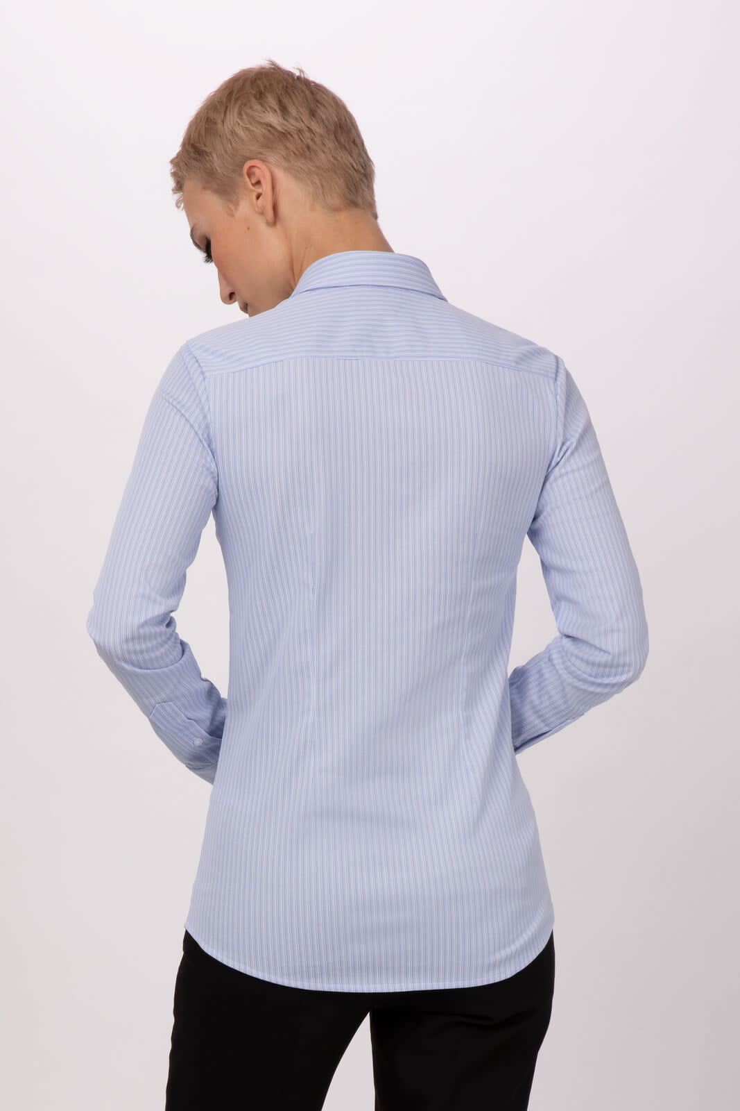 A women's shirt in light blue with a striped pattern, featuring a collar and long sleeves. The shirt has a branding logo.
