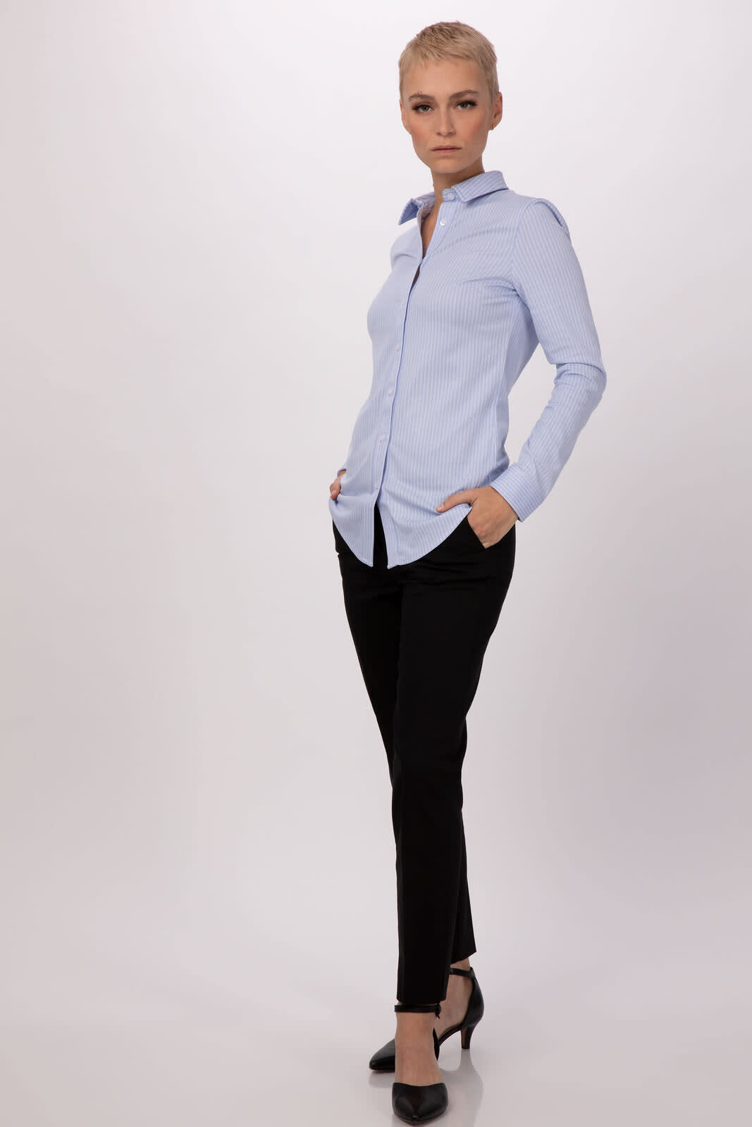 A light blue women's shirt with long sleeves and a collar, paired with black pants. The model has short hair.