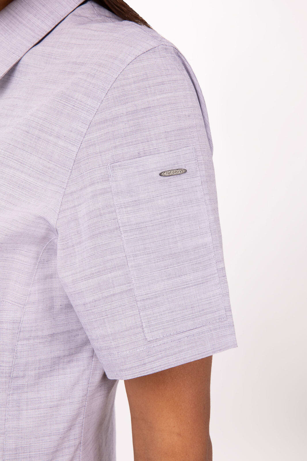 A short-sleeved women’s button-up shirt in light lavender with a branded logo on the sleeve.