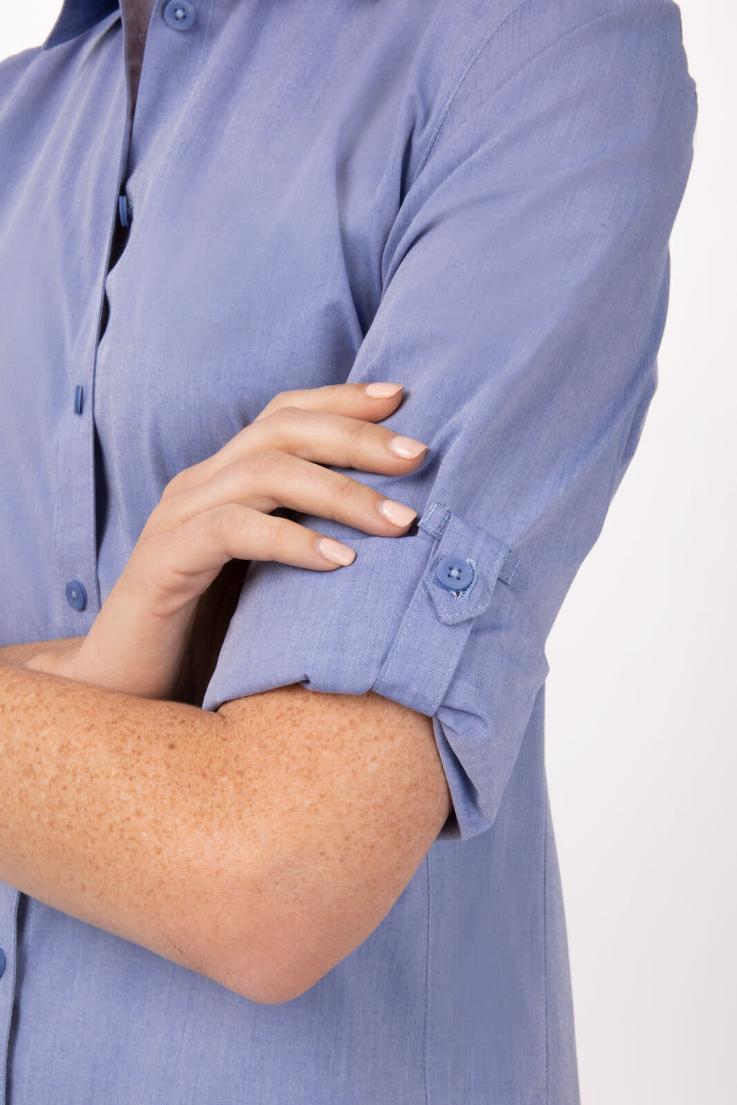 A blue chambray women's button-up dress shirt with rolled sleeves and a button detail.