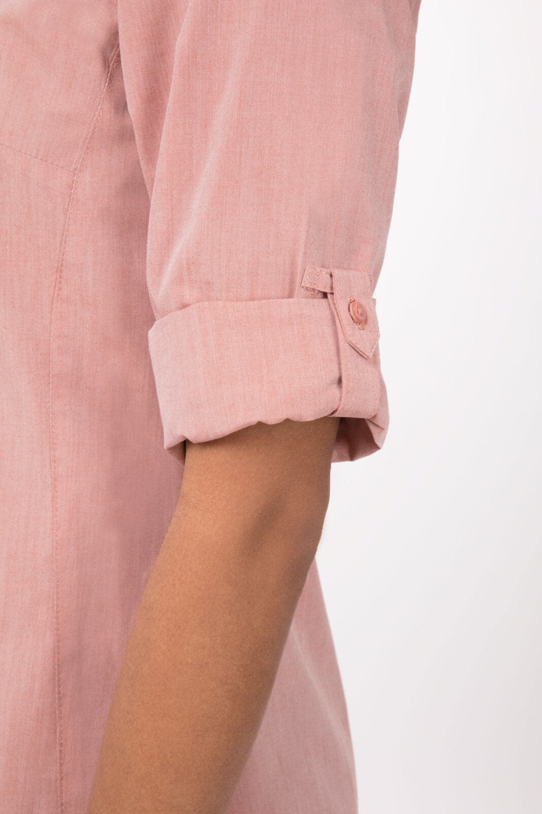 A close-up of a pink chambray women's dress shirt featuring rolled sleeves and a button detail.