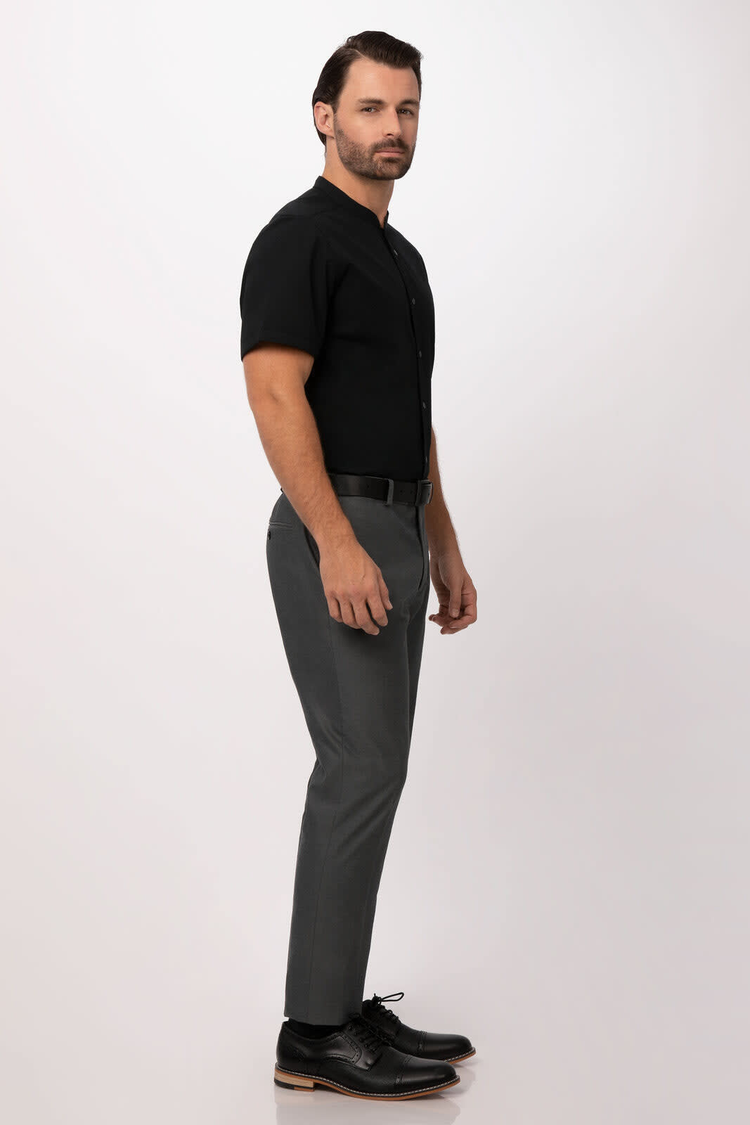 A man poses in a fitted black button-up shirt and grey trousers, featuring a sleek silhouette.