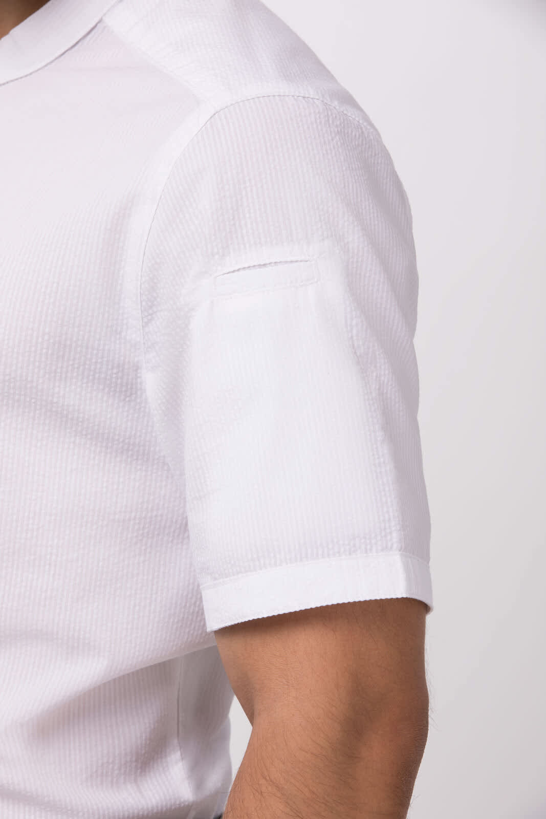 A white seersucker button-up shirt with a short sleeve and a pocket on the arm. Includes a branding logo.