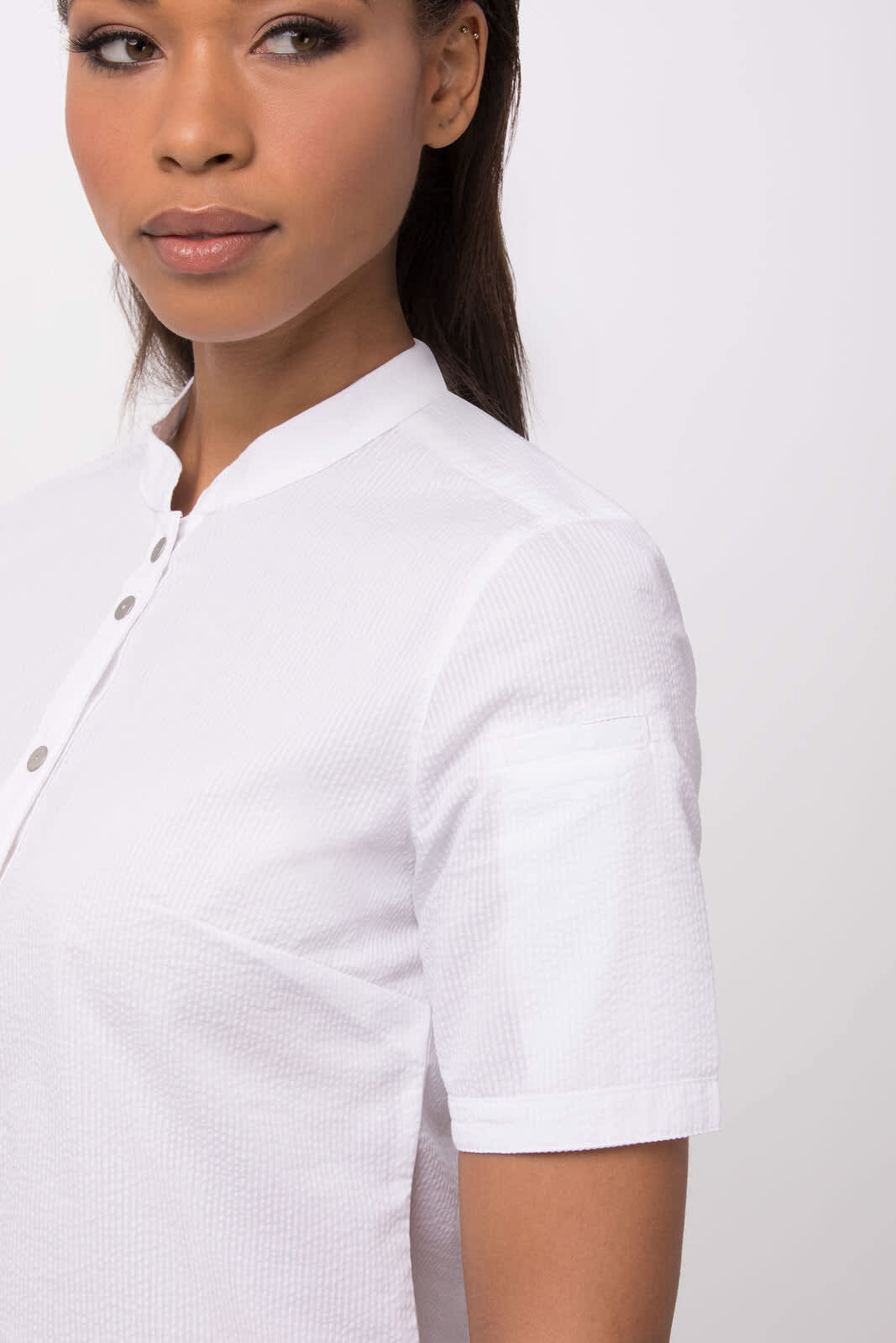 A white seersucker women's button-up shirt with short sleeves and a mandarin collar, featuring a logo.