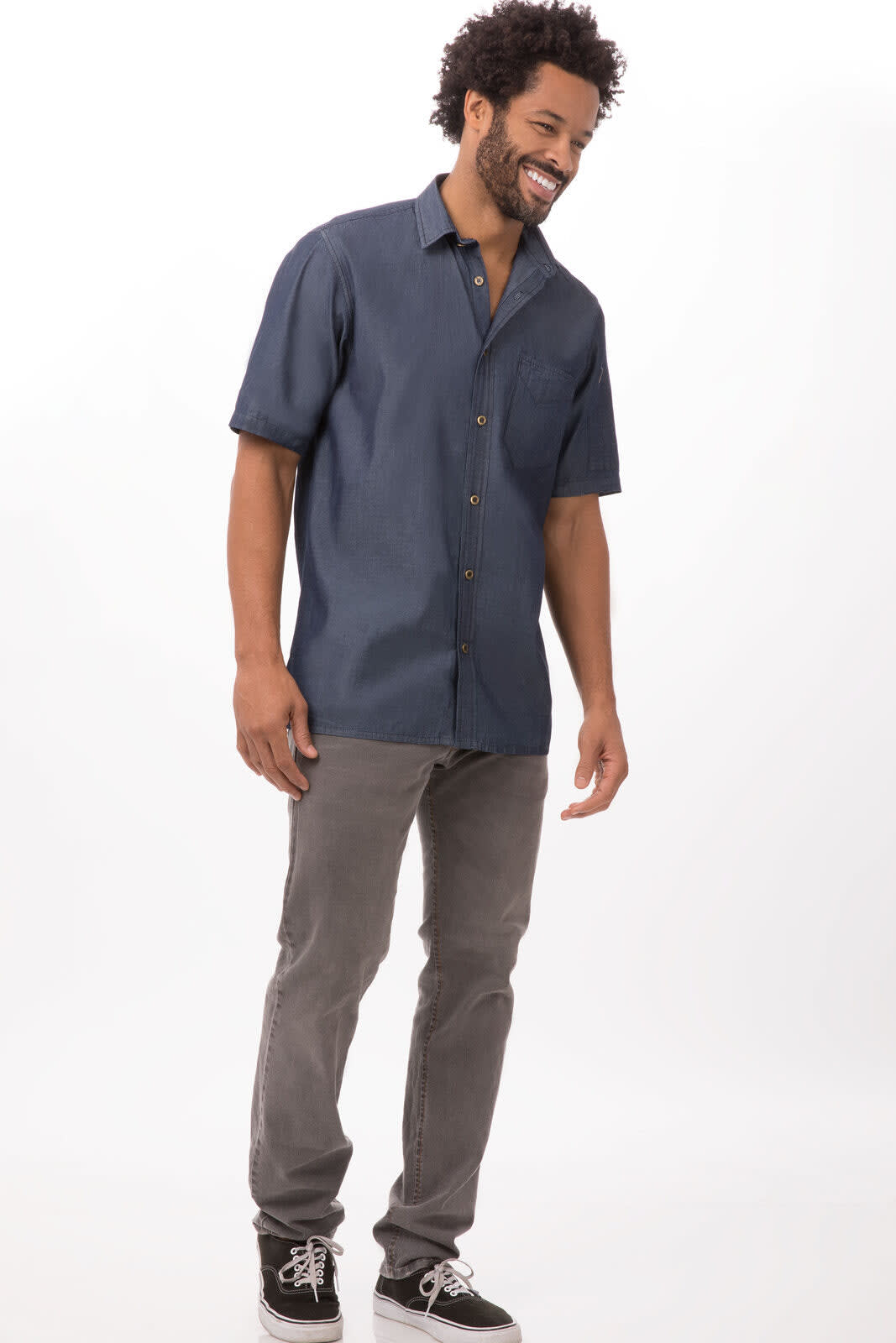 A man wearing a short sleeve denim button-up shirt in navy blue, paired with grey pants and black shoes.
