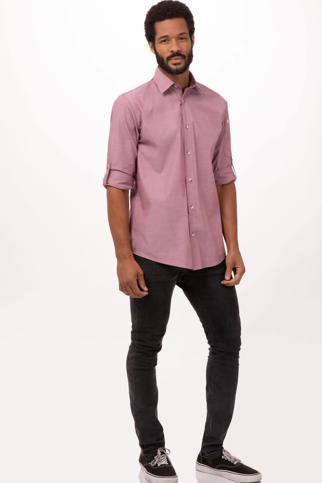 A man wearing a light purple chambray button-up shirt, paired with black jeans and shoes. The shirt has a logo.