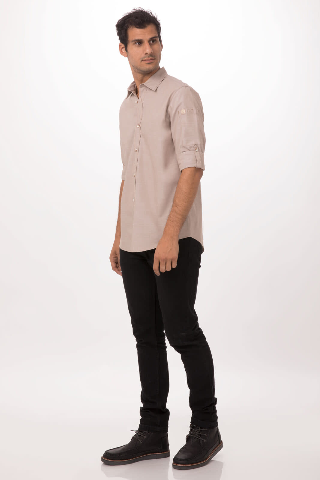 A man wearing a light brown chambray button-up shirt, paired with black jeans and dark shoes, standing casually.