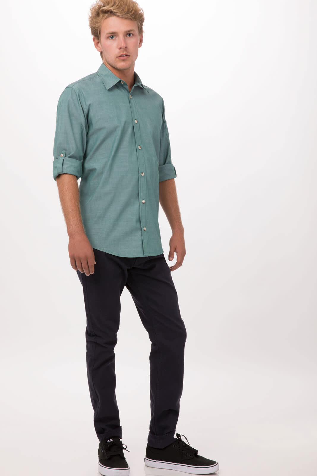 A green chambray men's button-up shirt is worn by a standing model, paired with dark trousers and black shoes.