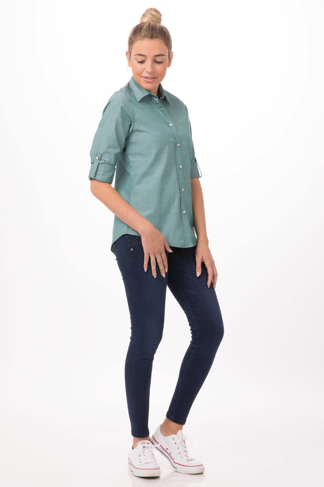 A chambray women's shirt in a light teal colour, paired with navy jeans and white sneakers, with a stylish casual pose.