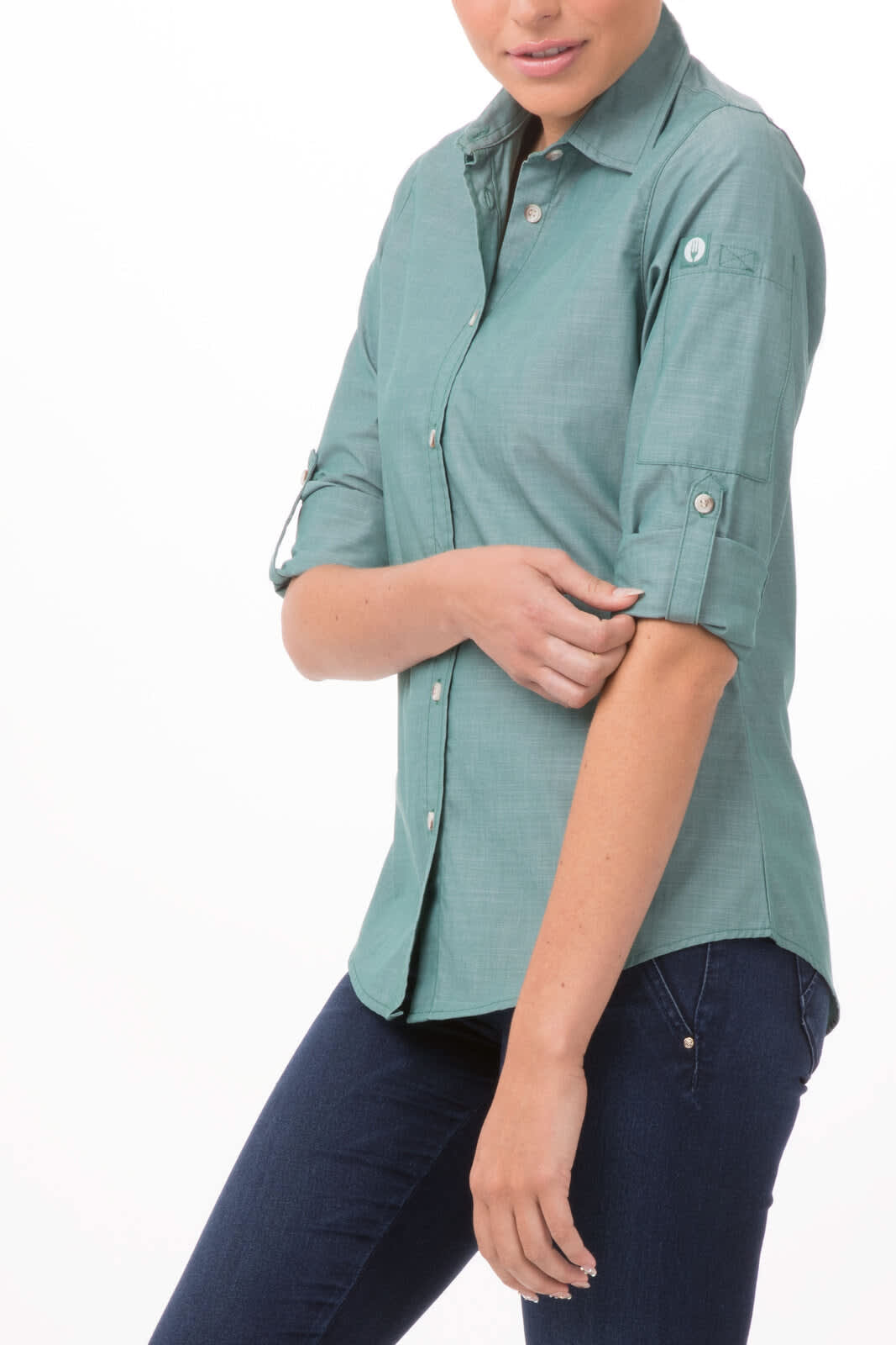 A chambray women's shirt in teal, featuring a button-up design and rolled-up sleeves. The model is wearing it with jeans.