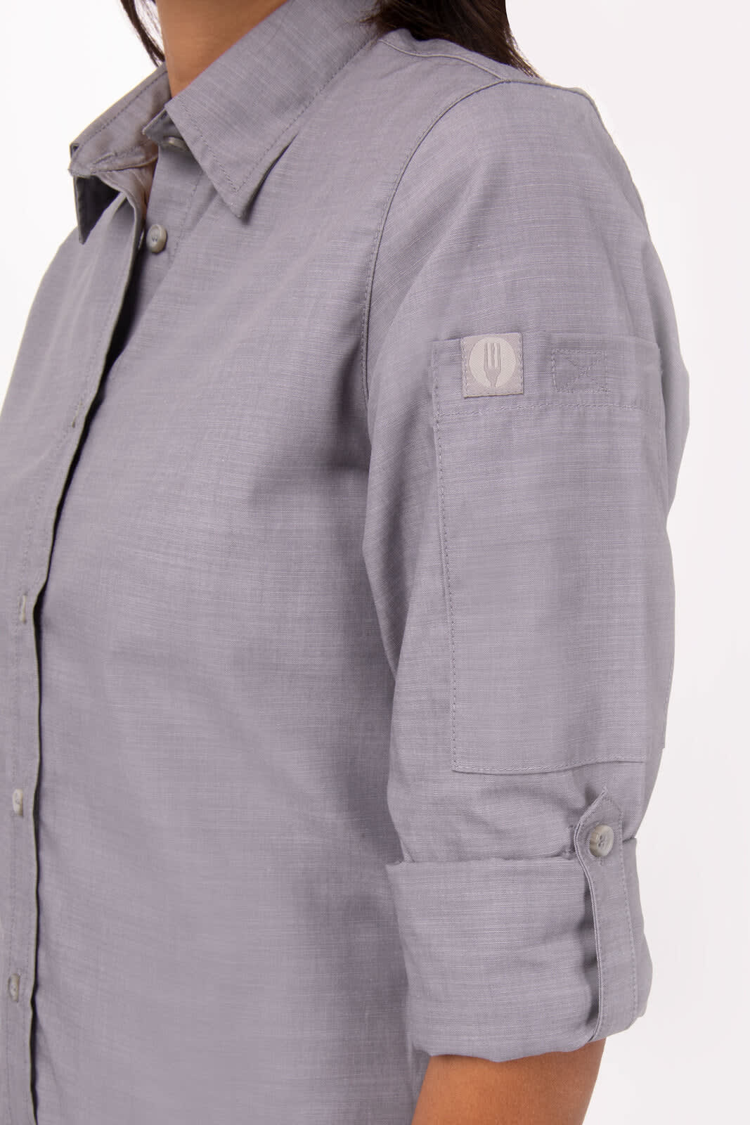 A grey chambray women's shirt with rolled sleeves and a logo on the arm.