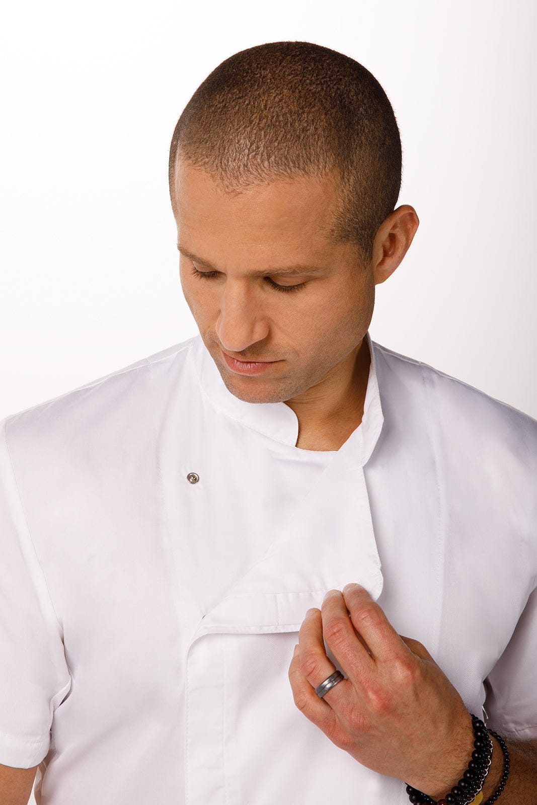 A chef wearing a white Cannes Press Stud Chef Jacket, adjusting the collar, with a logo visible.