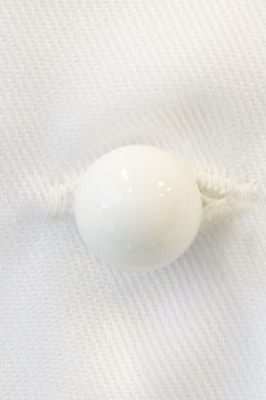A white stud button on a white fabric background, featuring a glossy finish and a simple round shape.