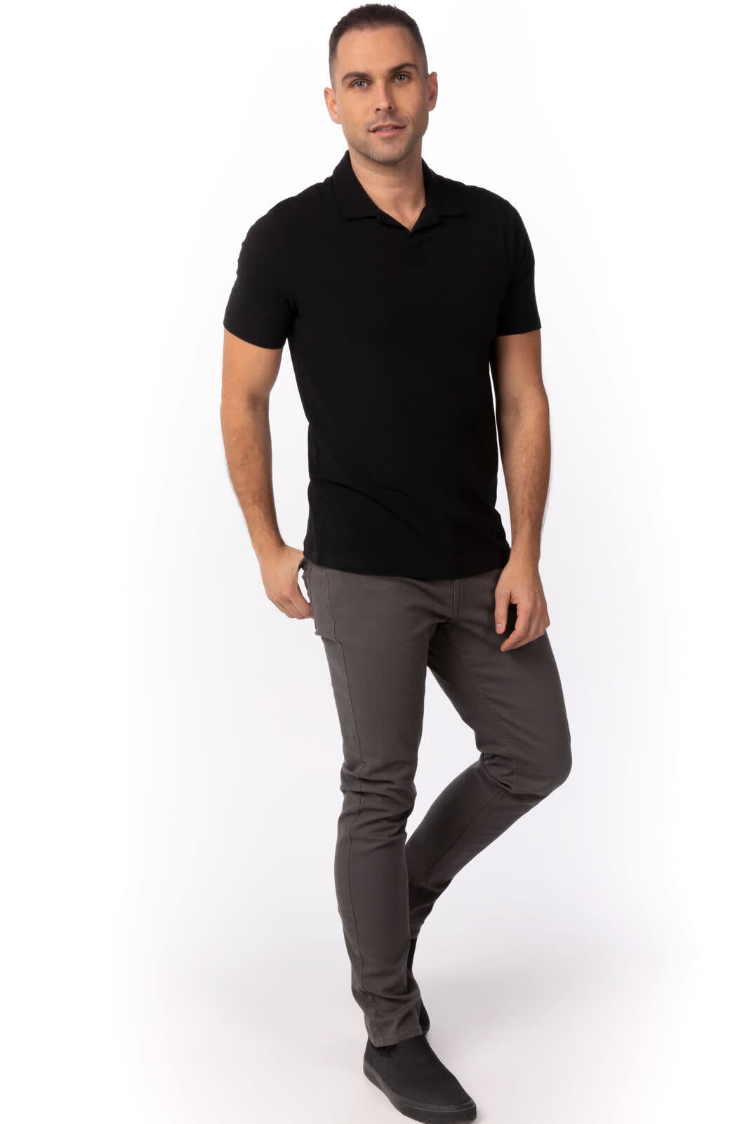 A black polo shirt displayed on a model, paired with grey trousers and black shoes. The shirt features a logo.